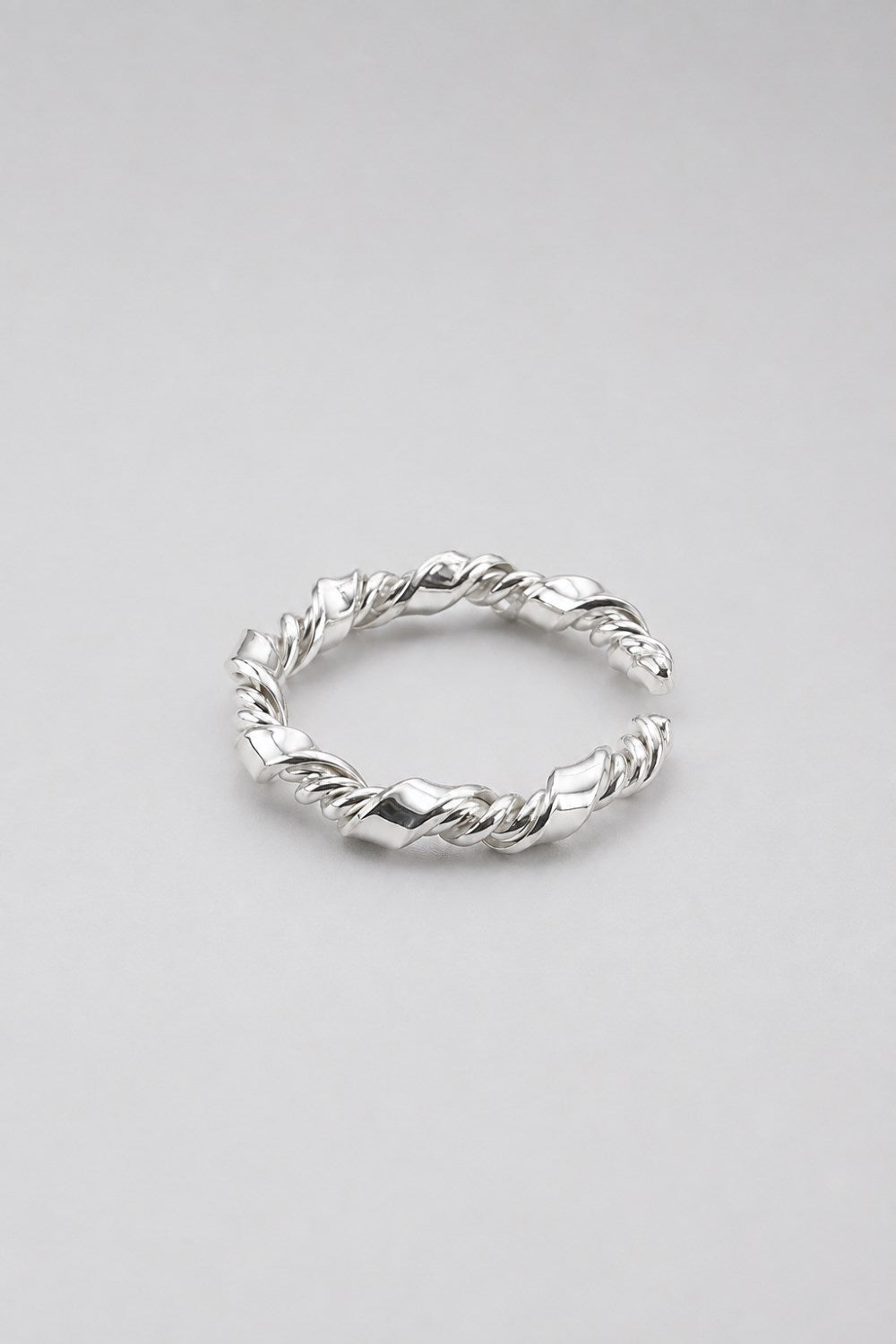 A silver twisted rope ring with a textured, braided design, photographed on a neutral light gray background.