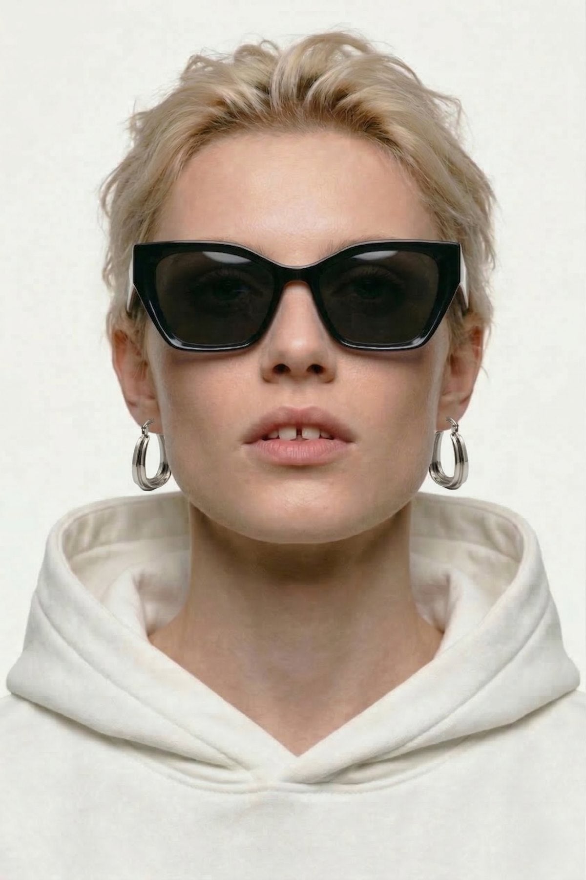 Person wearing black sunglasses and a white hoodie on a plain background