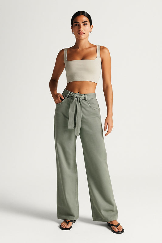 Woman wearing a beige crop top and green high-waisted pants on a white background
