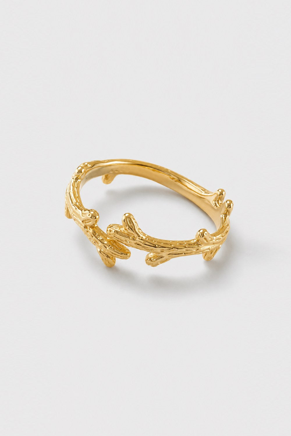 A gold ring designed to look like textured tree branches or coral, photographed on a clean, light gray background.
