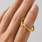 A close-up of a hand wearing a textured gold ring designed to look like a small branch or antler, set against a soft light gray background.