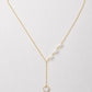 A delicate gold Y-necklace featuring a row of white pearls on one side and a small gold heart pendant with a white inlay on the other, displayed on a light gray background.