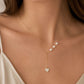 A close-up of a model wearing a delicate gold Y-necklace with three small white pearls and a heart-shaped pearl pendant, paired with a cream satin top.