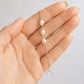A delicate silver chain bracelet with three white freshwater pearls and a small open heart charm, held in a person's hand against a light gray background.