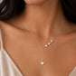 A close-up of a woman wearing a delicate silver Y-necklace with three small pearls and a heart-shaped pendant, paired with a beige satin top.