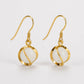 A pair of gold-tone dangle earrings with circular white stone bezels, shown on a clean white background.