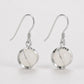 A pair of silver-toned dangle earrings with oval milky white stone drops, shown on a clean light gray background.
