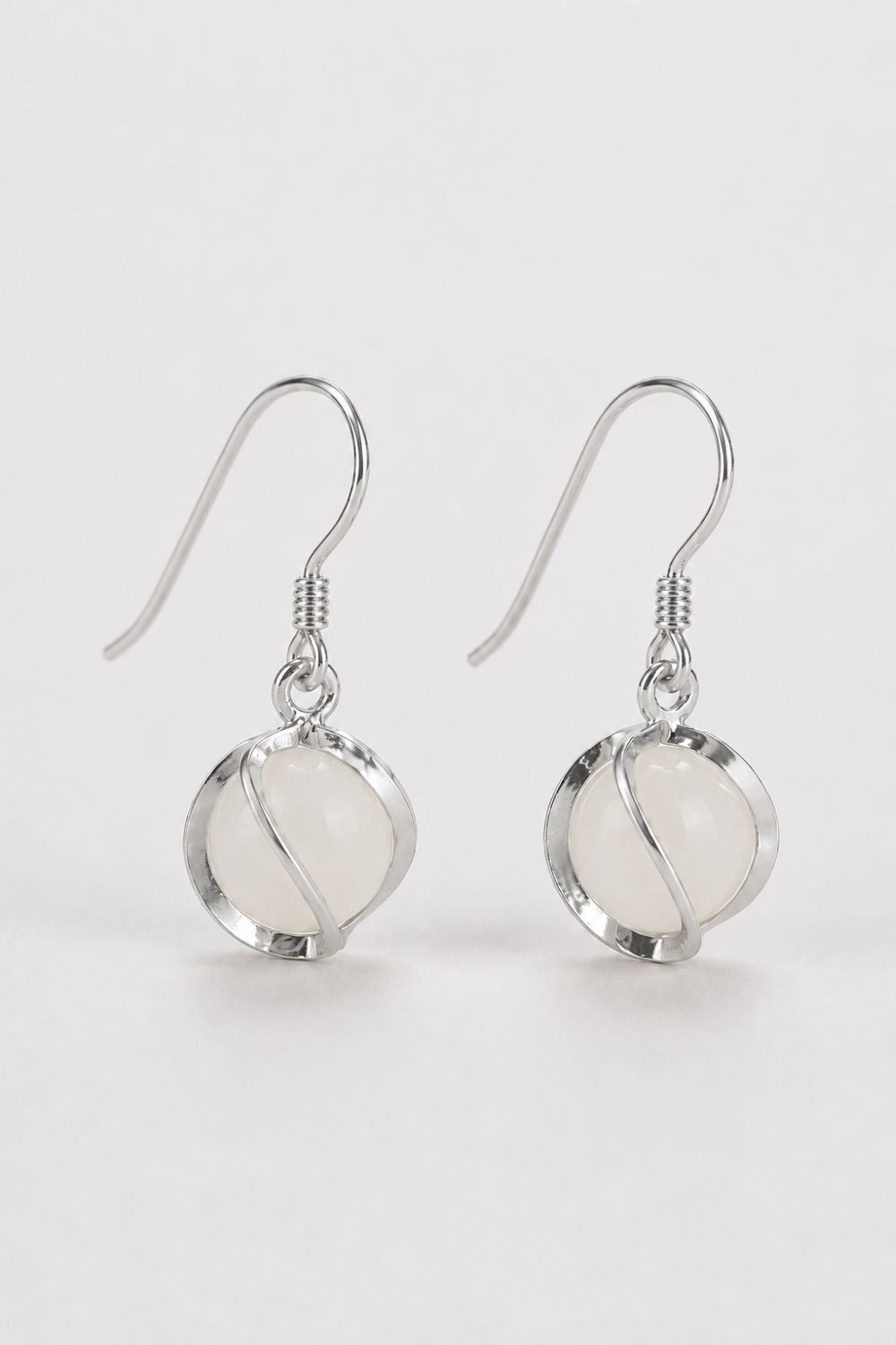 A pair of silver-toned dangle earrings with oval milky white stone drops, shown on a clean light gray background.