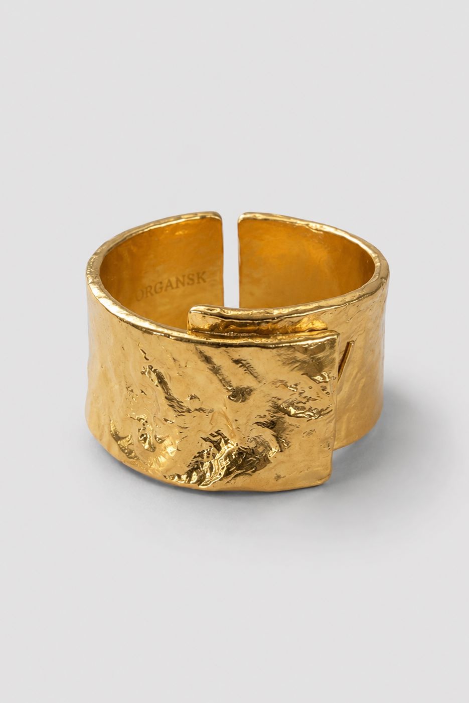 A textured gold open cuff ring with a hammered, organic surface finish, shown on a neutral light gray background. The brand name 'ORGANSK' is subtly engraved inside the band.