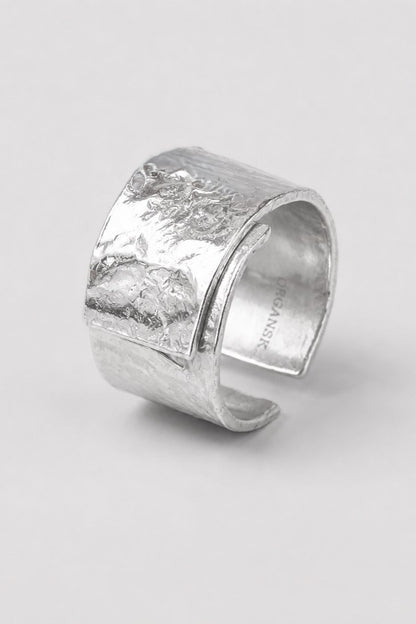 A wide, chunky silver cuff ring with a heavily textured, hammered finish, photographed on a neutral light gray background.