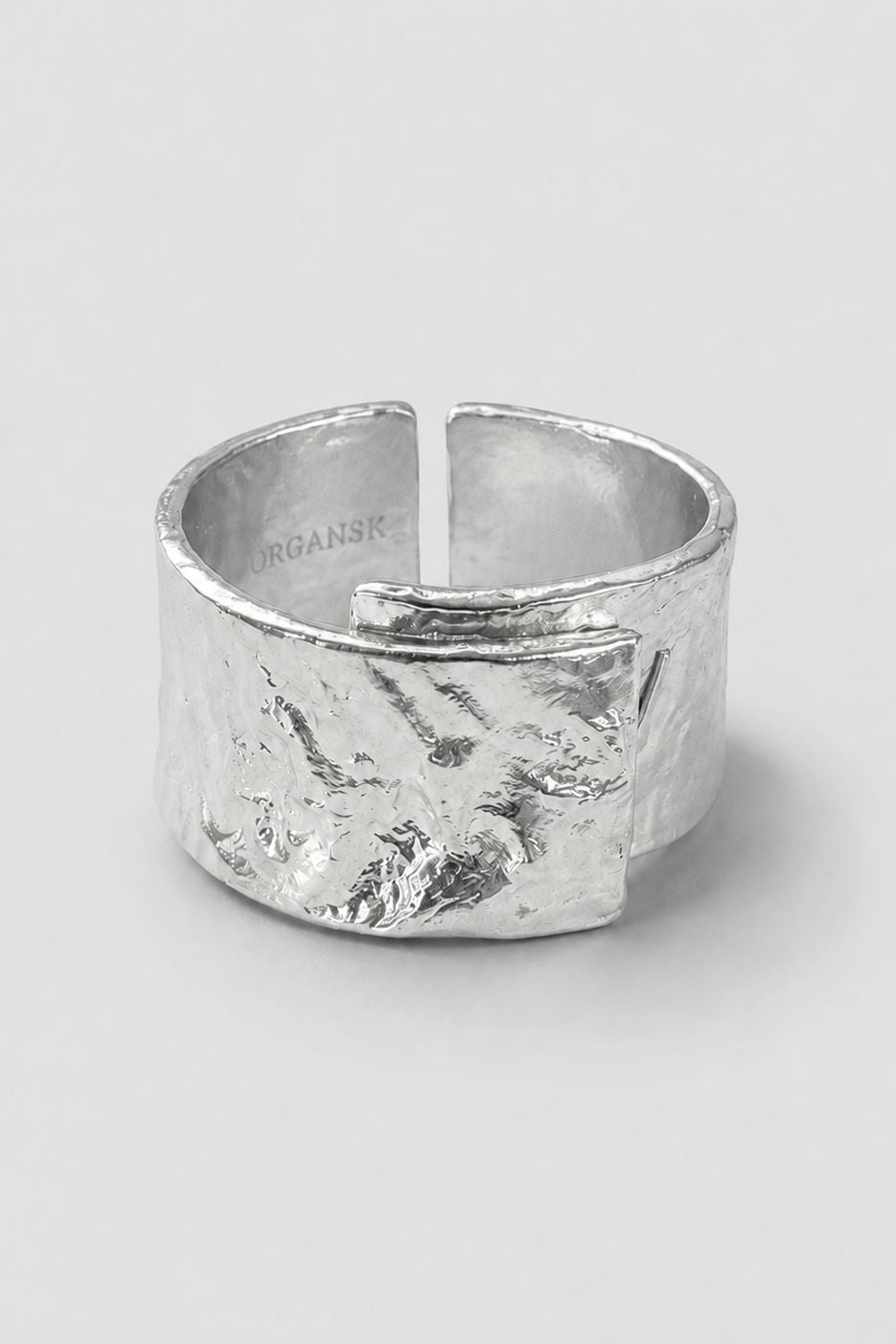 A wide, textured silver ring with a hammered organic finish and an open split design, photographed on a neutral light gray background.