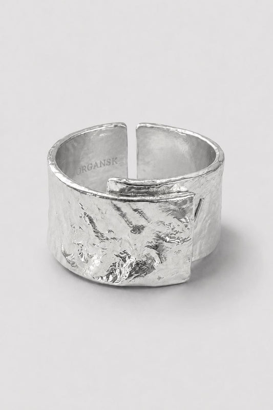 A wide, textured silver ring with a hammered organic finish and an open split design, photographed on a neutral light gray background.