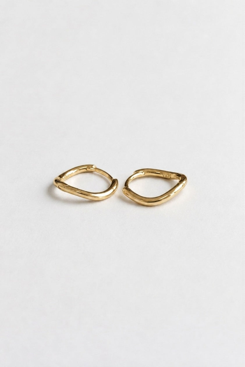 A pair of small gold huggie hoop earrings with a textured, organic wavy outline, displayed on a clean white background.