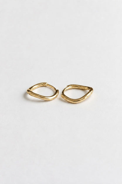 A pair of small gold huggie hoop earrings with a textured, organic wavy outline, displayed on a clean white background.