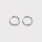 A pair of polished silver-toned metal hoop earrings with a unique twisted, organic loop design, displayed on a clean, light gray background.