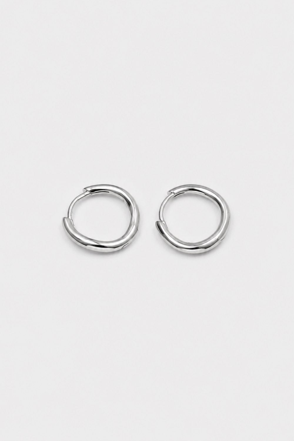 A pair of polished silver-toned metal hoop earrings with a unique twisted, organic loop design, displayed on a clean, light gray background.