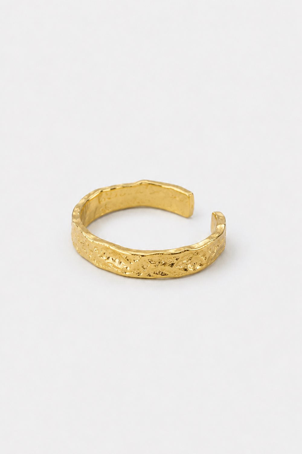 A textured gold open cuff ring with a hammered, organic surface finish, displayed on a clean white background.