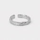 A textured silver open cuff ring with a hammered, organic surface pattern, displayed on a clean light gray background.