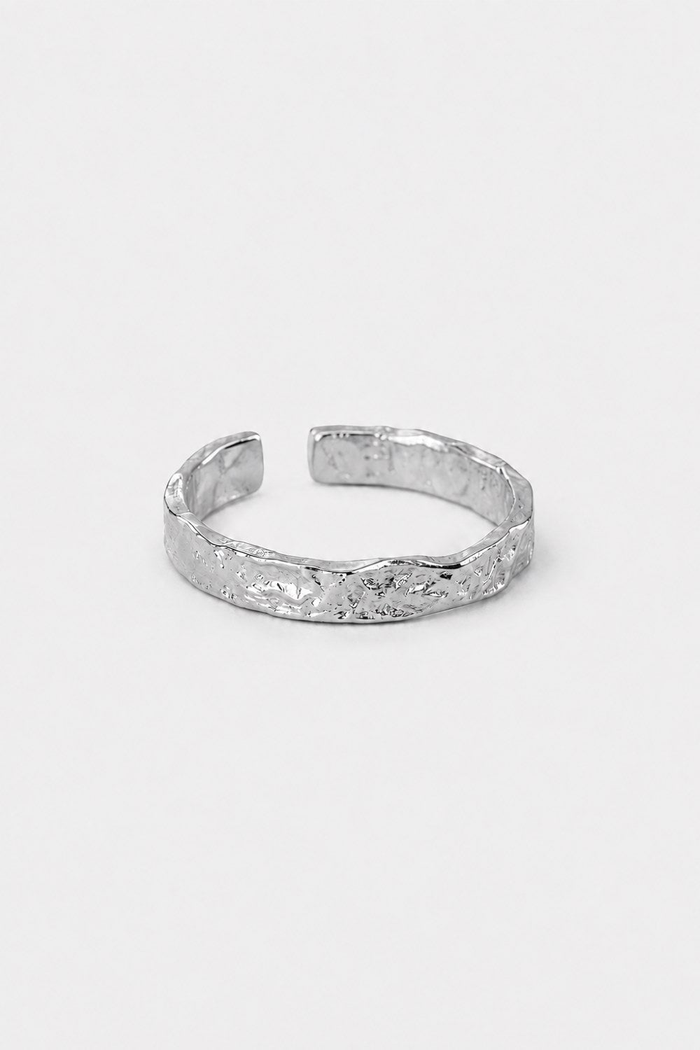 A textured silver open cuff ring with a hammered, organic surface pattern, displayed on a clean light gray background.