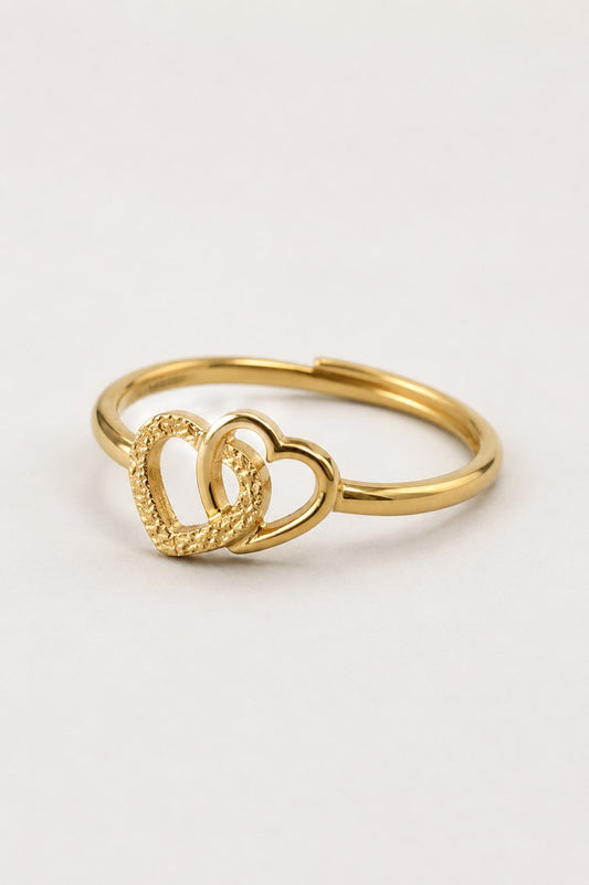 A gold ring featuring two interlocking open heart designs, one with a smooth polished finish and the other with a textured, rope-like border, set against a plain light background.