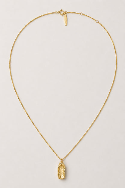 A delicate gold chain necklace with a small, vertically oriented oval-cut gold pendant, displayed on a clean, light gray background.