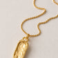 A gold necklace with a textured, irregularly shaped pendant, displayed on a light off-white textured background.