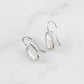 A pair of silver drop earrings with oval iridescent white inlay stones, displayed on a light gray marble surface.