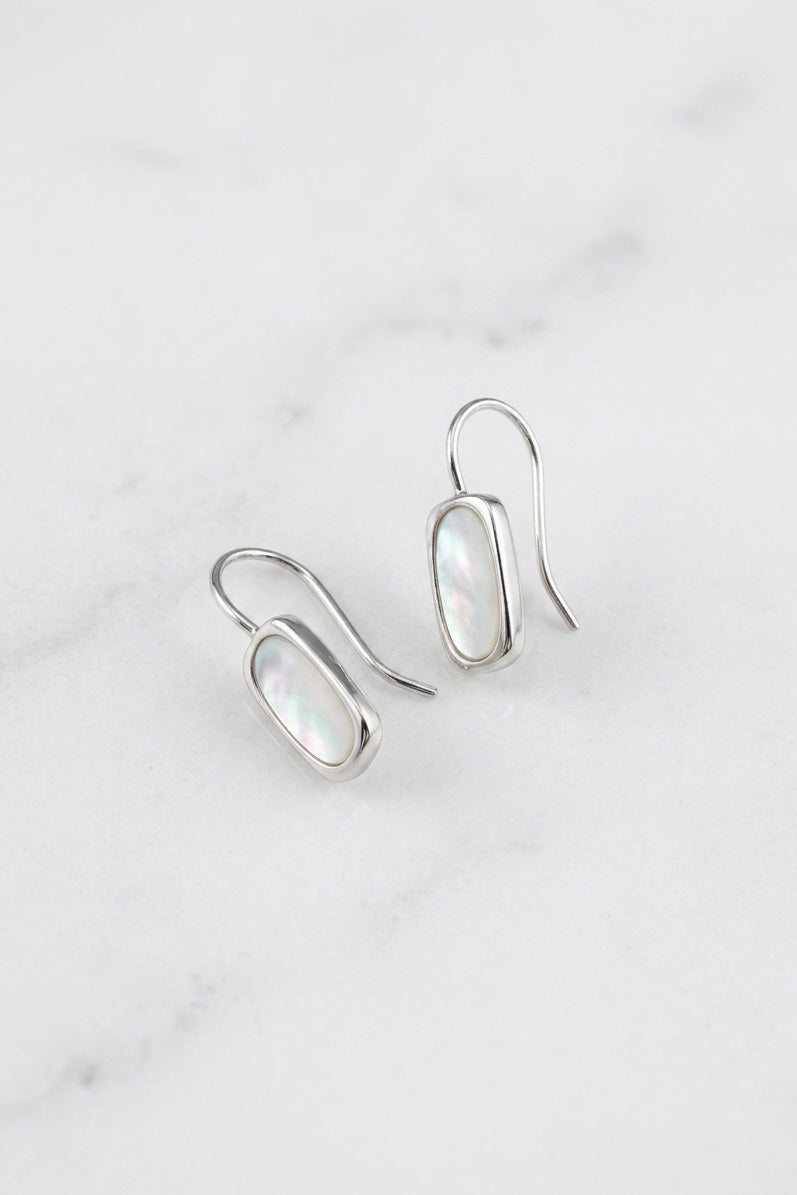 A pair of silver drop earrings with oval iridescent white inlay stones, displayed on a light gray marble surface.