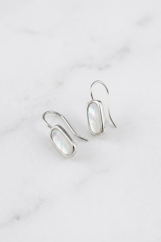 A pair of silver drop earrings with oval iridescent white inlay stones, displayed on a light gray marble surface.