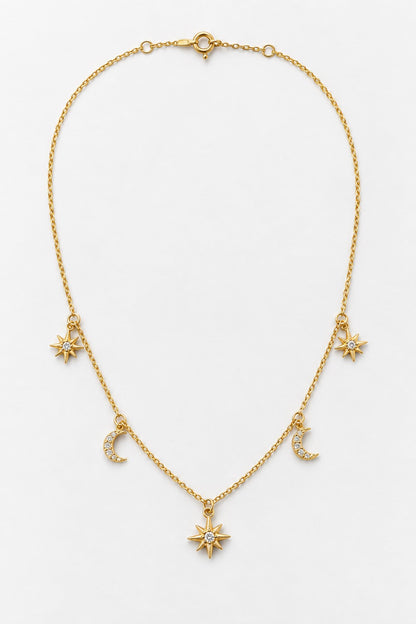 A delicate gold chain necklace featuring celestial charms, including a central sunburst pendant, two crescent moons, and two starbursts, displayed on a clean white background.