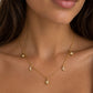 A close-up of a model wearing a delicate gold necklace with small celestial charms, including three crescent moons and three starburst pendants, arranged in a Y-shape.