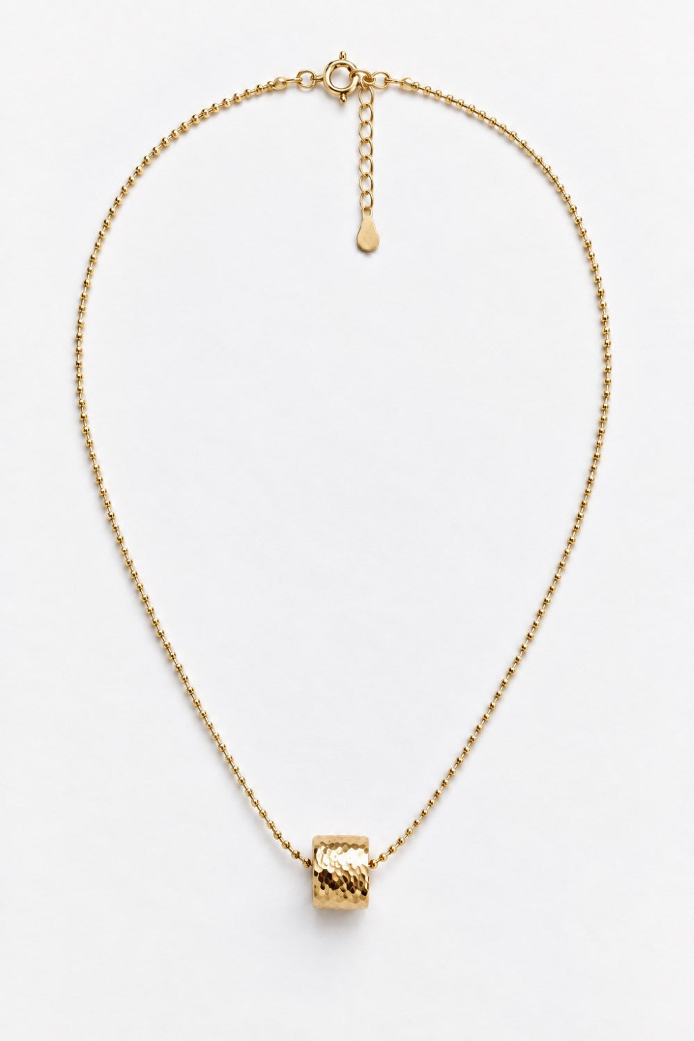 A delicate gold chain necklace with a textured cylindrical pendant, displayed on a clean white background.
