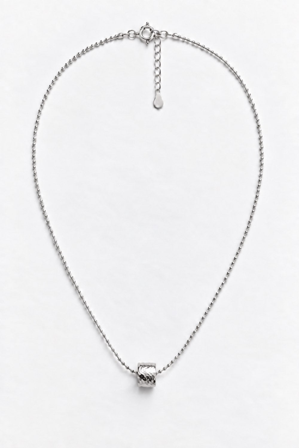 A silver chain necklace with a small textured geometric pendant, displayed on a clean white background.