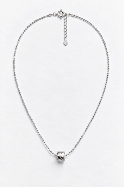 A silver chain necklace with a small textured geometric pendant, displayed on a clean white background.
