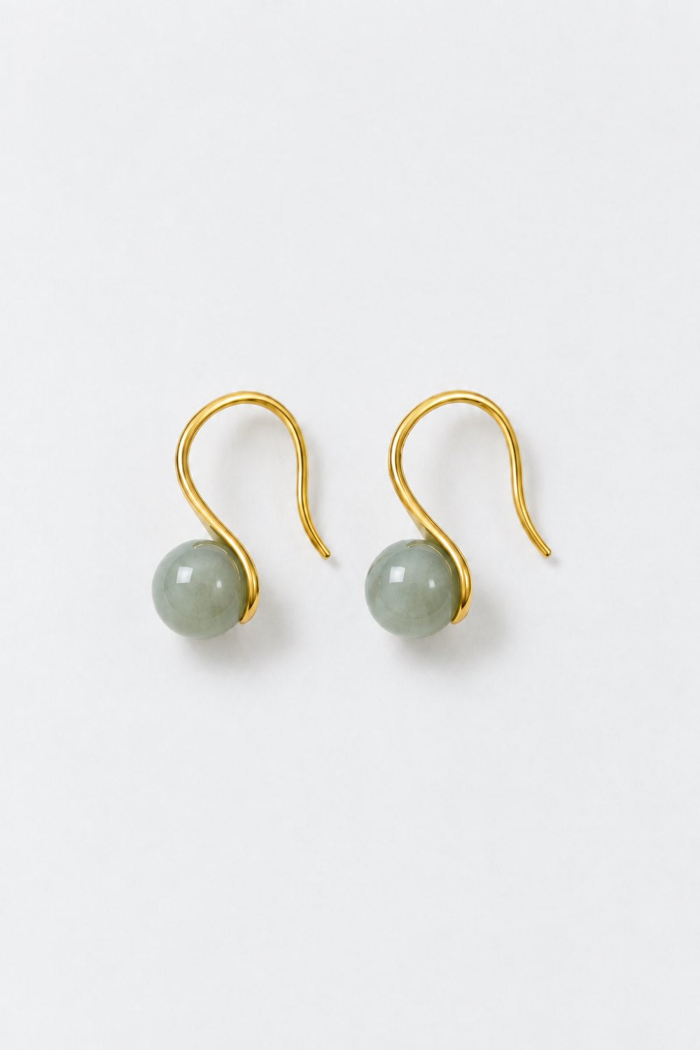 A pair of gold S-shaped dangle earrings with smooth, pale green bead drops, displayed on a clean white background.