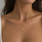 A close-up of a model wearing a delicate gold chain necklace with a crescent moon pendant, styled with a white ribbed tank top.