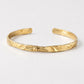 A textured gold cuff bracelet with an open, adjustable design, photographed on a clean white background.