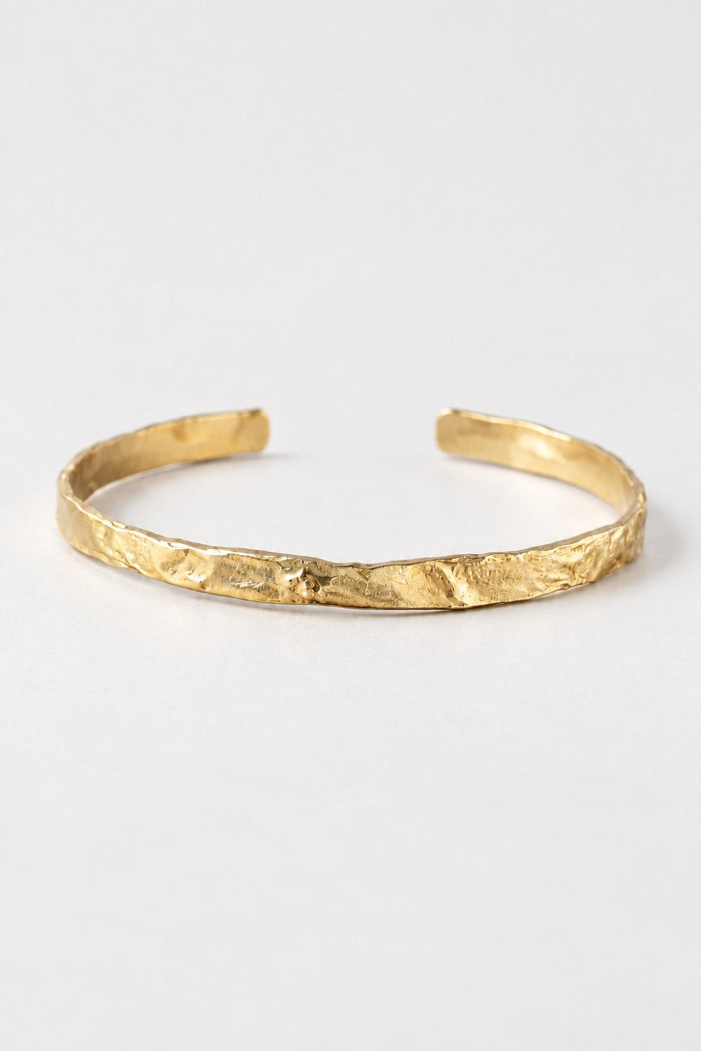 A textured gold cuff bracelet with an open, adjustable design, photographed on a clean white background.