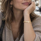 A woman wearing black cat-eye sunglasses, a gold hoop earring, and a gold bangle bracelet, posing outdoors in a beige knit sweater.