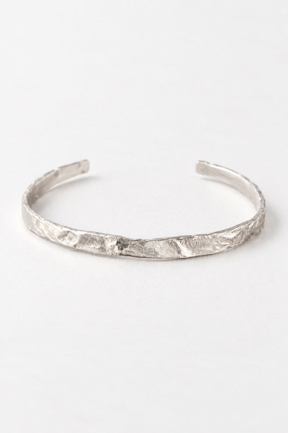 A textured silver cuff bracelet with an organic, hammered surface, displayed on a clean white background.