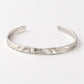 A textured silver cuff bracelet with an organic, hammered surface, displayed on a clean white background.