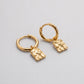 A pair of gold huggie hoop earrings with textured, irregularly shaped dangling charms, displayed on a clean light gray background.