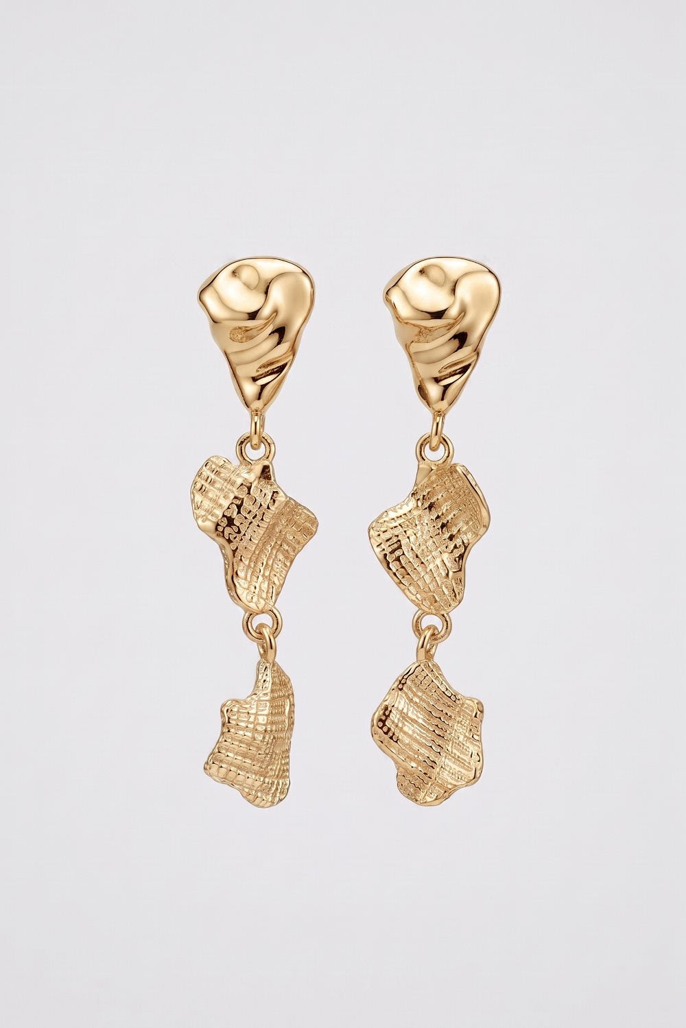 A pair of gold dangle earrings with organic, textured shell-like drops, shown against a light gray background.