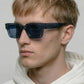 Person wearing dark sunglasses and a white hoodie against a plain background