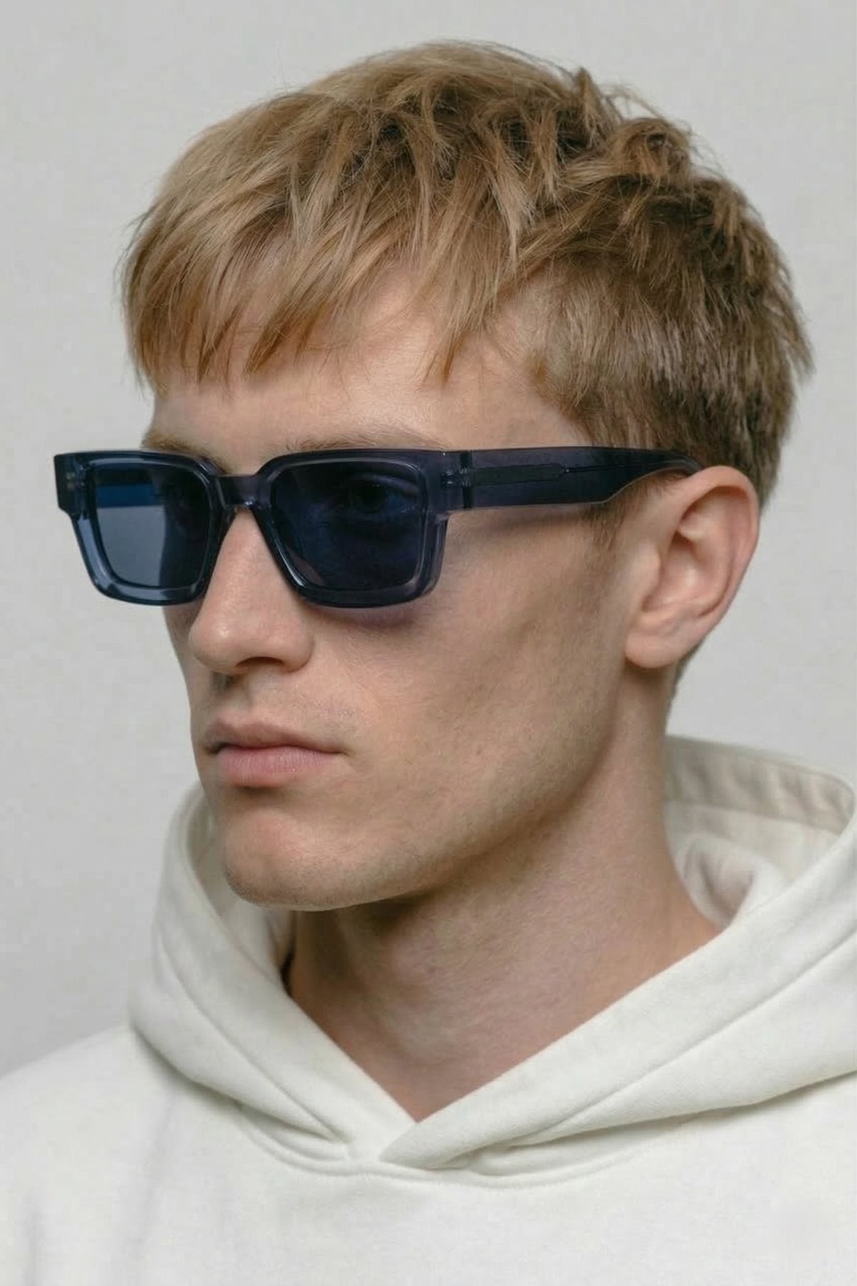 Person wearing dark sunglasses and a white hoodie against a plain background