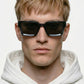 Person wearing dark blue ORGANSK  sunglasses and a white hoodie against a light background