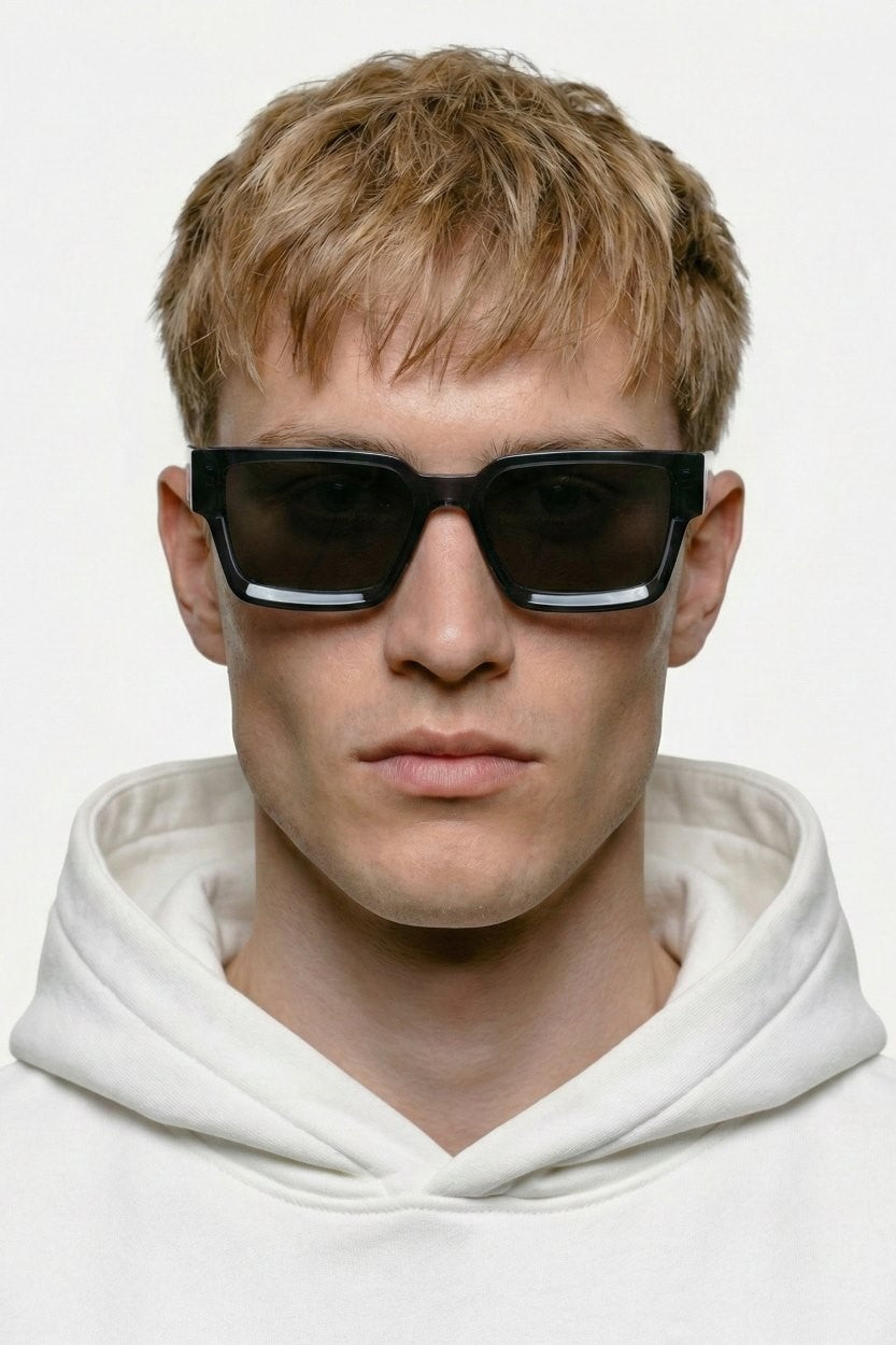 Person wearing dark blue ORGANSK  sunglasses and a white hoodie against a light background