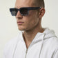 Man wearing dark sunglasses and a white hoodie against a light background