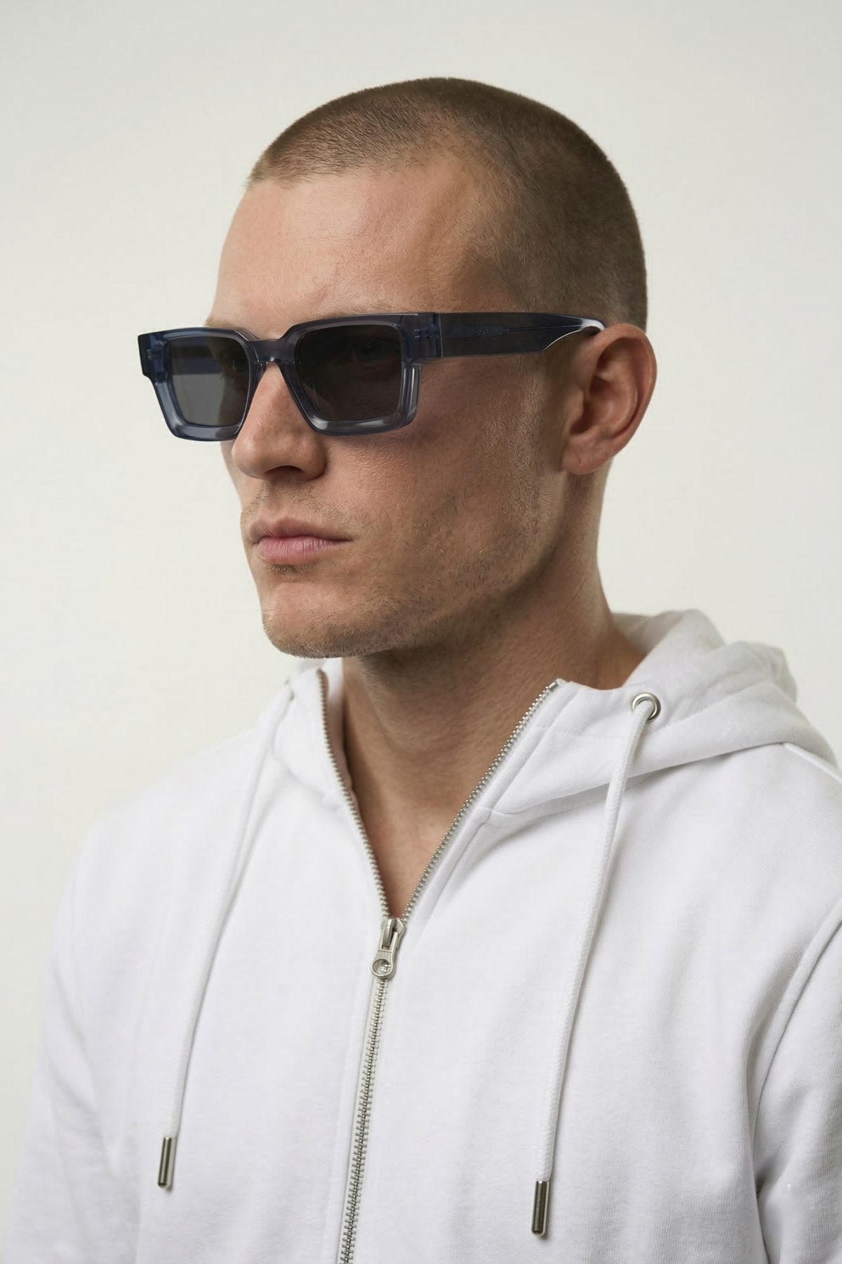 Man wearing dark sunglasses and a white hoodie against a light background