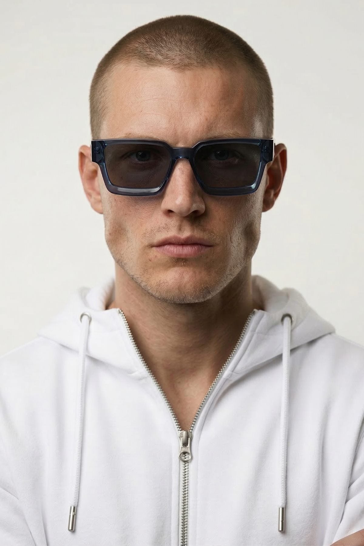 Man wearing dark sunglasses and a white hoodie against a light background